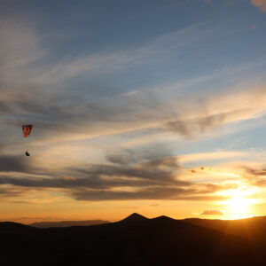 Gleitschirmflieger schwebt über Berggipfeln im Gegenlicht eines Sonnenuntergangs