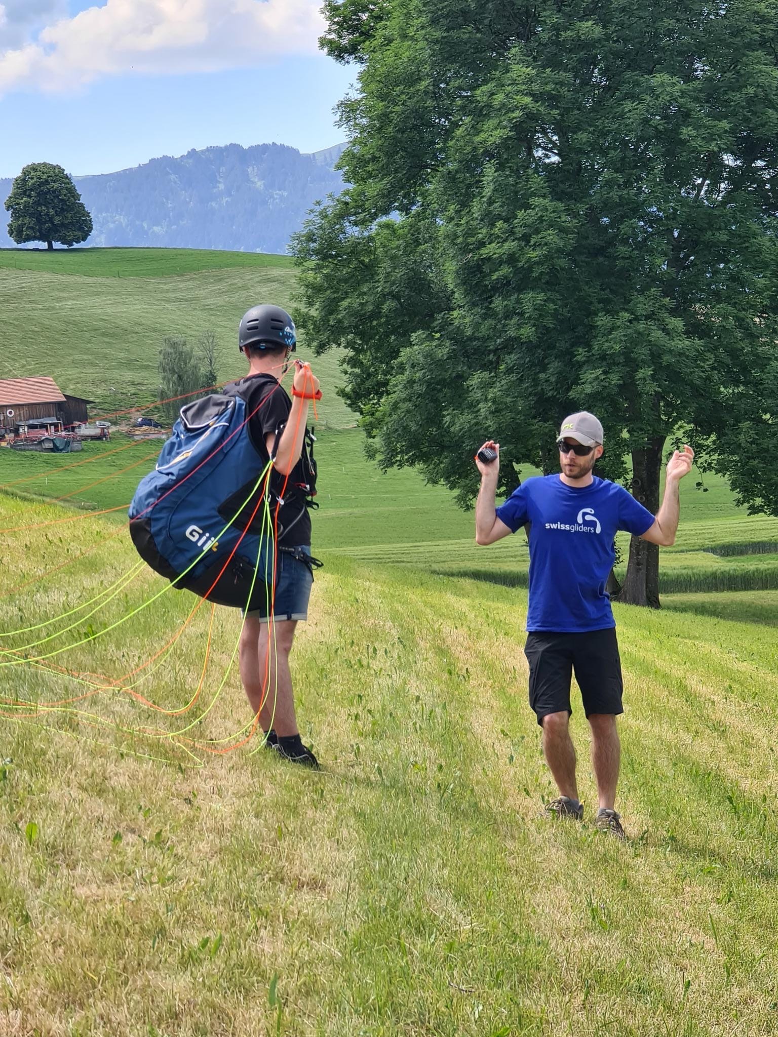 Fluglehrer von Swissgliders erklärt einem Schüler mit Gleitschirmleinen die Handhabung auf einer Wiese