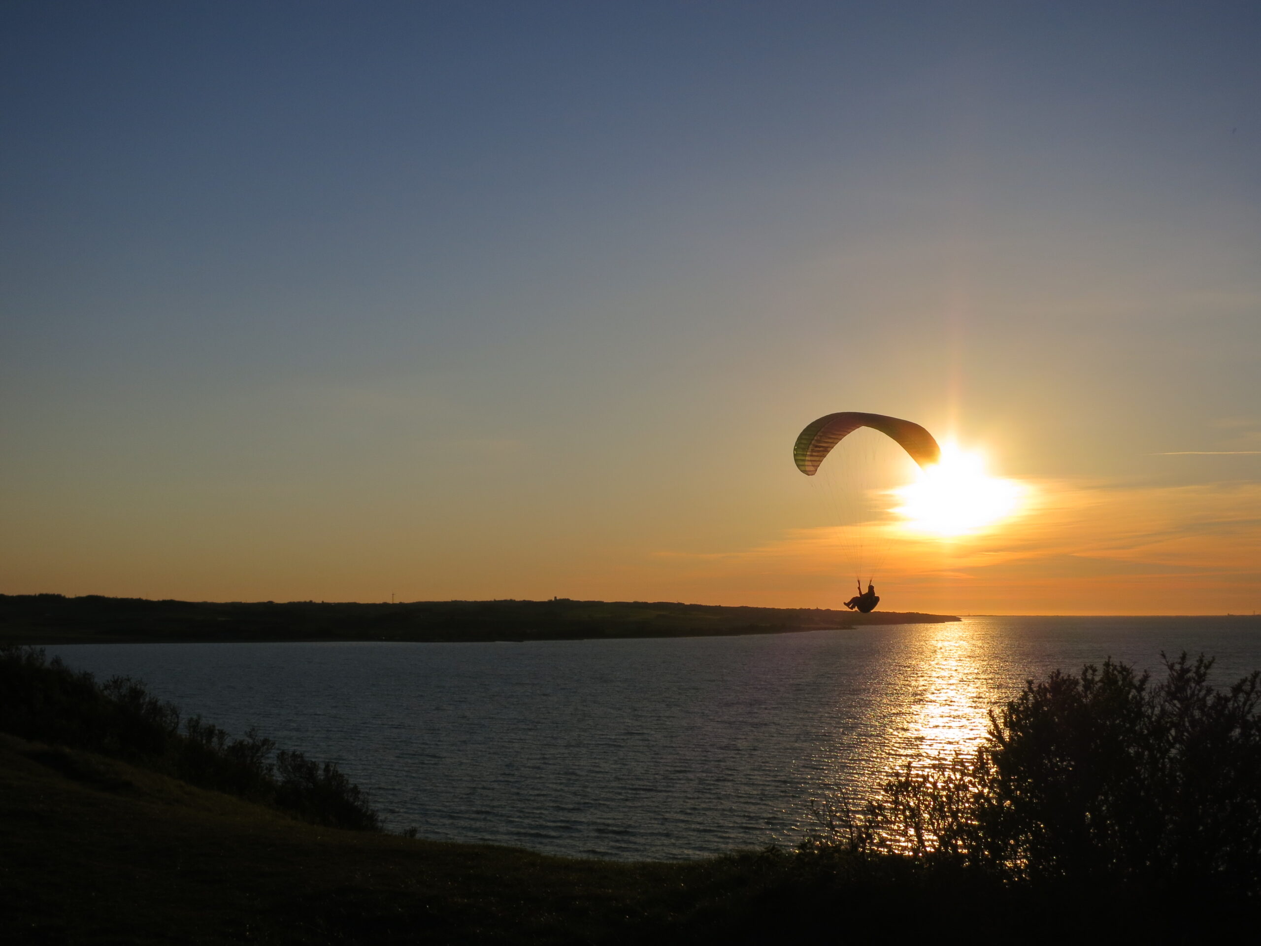 Gleitschirmpilot soart bei Sonnenuntergang entlang der dänischen Küste