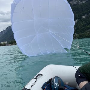 Weißer Gleitschirm treibt auf dem Wasser vor einem Schlauchboot, im Hintergrund bewaldete Berghänge