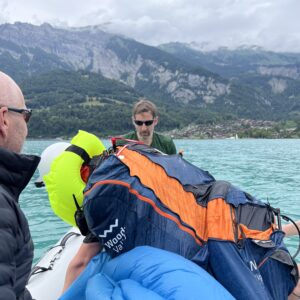 Männer bergen einen nassen Fallschirm auf einem Schlauchboot, im Hintergrund Bergsee und Alpen