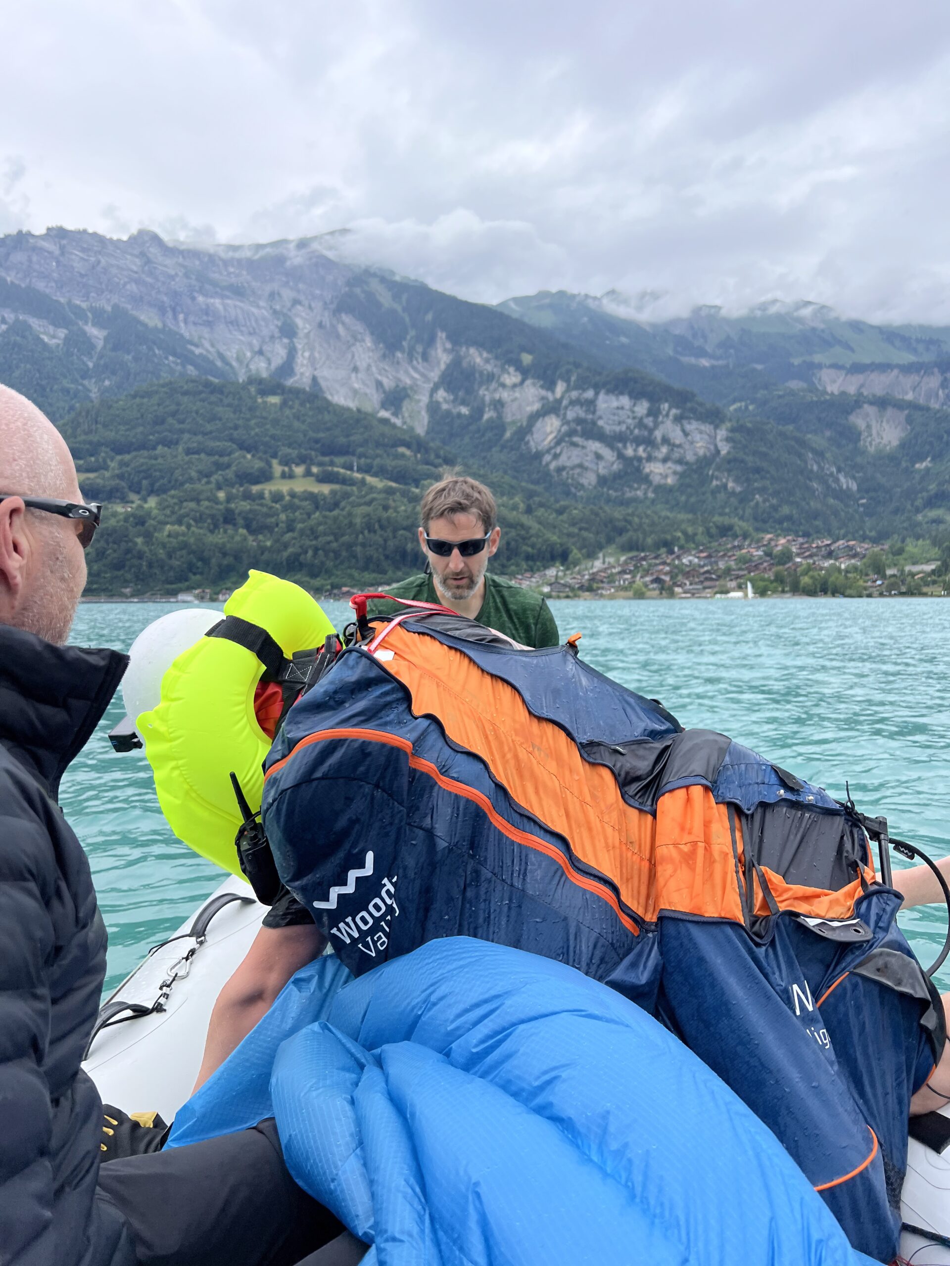 Männer bergen einen nassen Fallschirm auf einem Schlauchboot, im Hintergrund Bergsee und Alpen